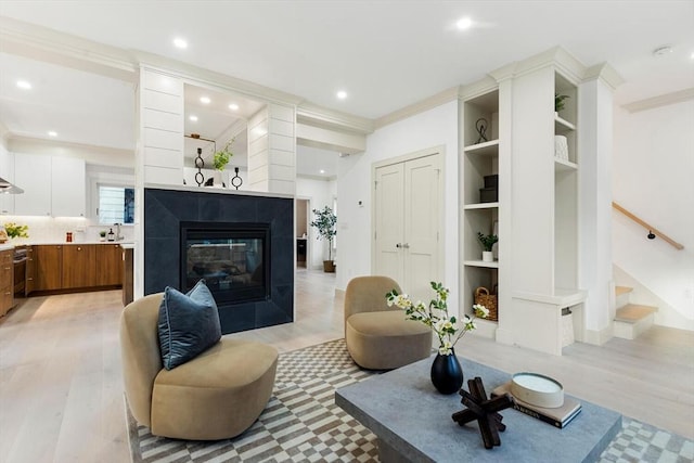 living room with a fireplace, light wood-type flooring, built in features, and ornamental molding