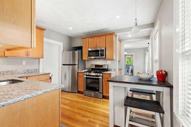 29 Daniels St Unit 29, Arlington, MA 02476 - kitchen featuring stainless steel appliances, light wood-style floors, light stone countertops, decorative light fixtures, and a sink