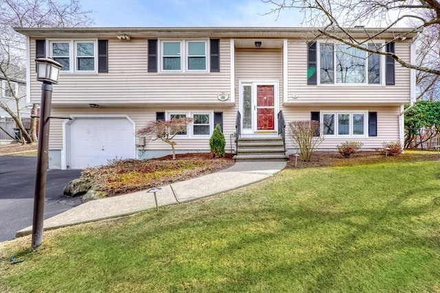 raised ranch with a garage, a front lawn, driveway, and fence