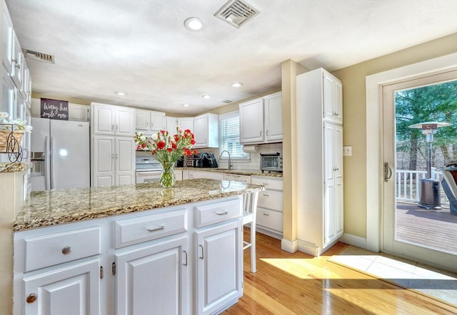 kitchen featuring a sink, visible vents, white fridge with ice dispenser, and white cabinets