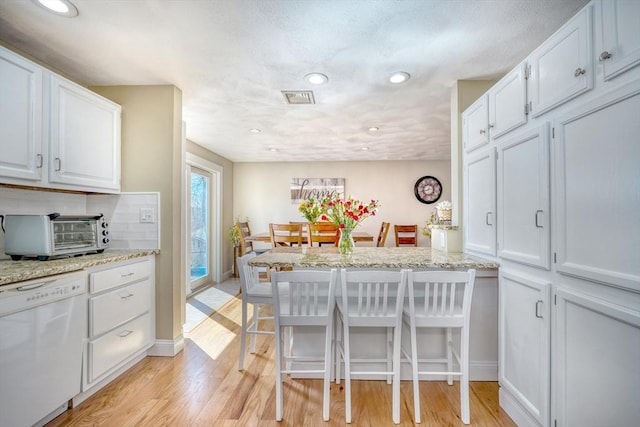 kitchen with visible vents, a toaster, light wood-style flooring, white dishwasher, and white cabinetry