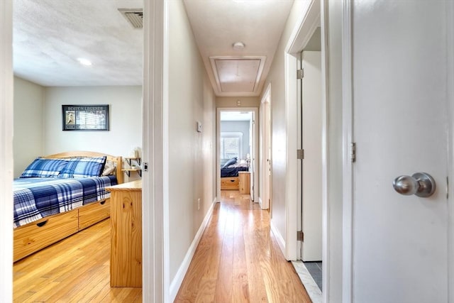 hall featuring baseboards, visible vents, attic access, and light wood-style floors