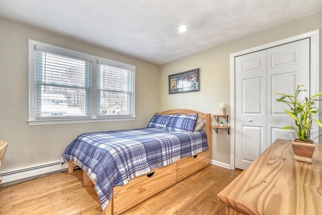 bedroom with a closet, baseboard heating, baseboards, and wood finished floors