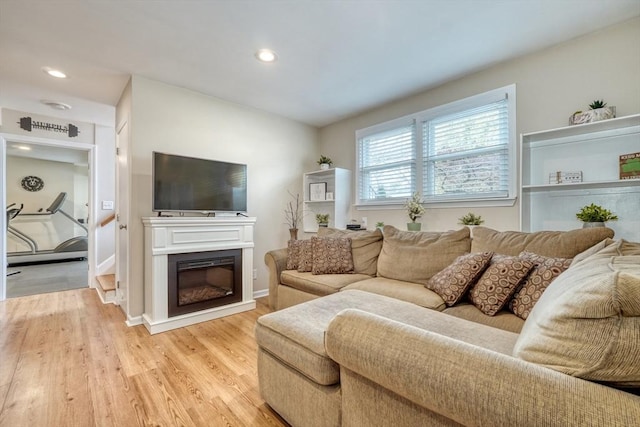 living area with a glass covered fireplace, recessed lighting, light wood-type flooring, and baseboards