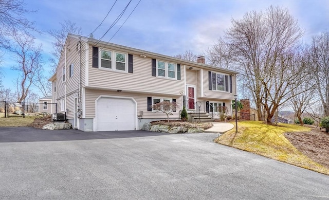 split foyer home featuring fence, central AC, a chimney, a garage, and driveway