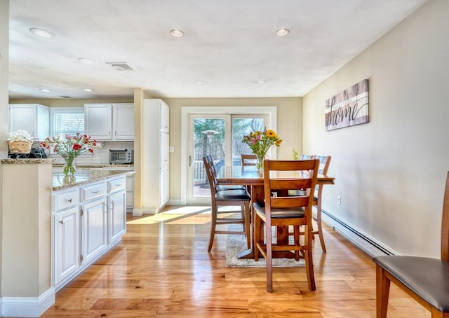 dining room with light wood finished floors, baseboard heating, a healthy amount of sunlight, and a toaster