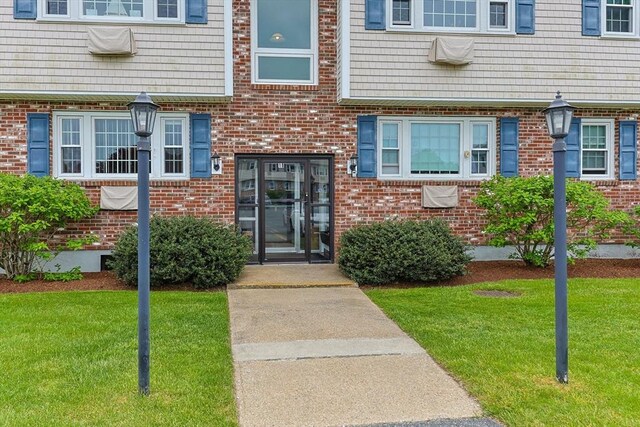 entrance to property featuring brick siding and a lawn