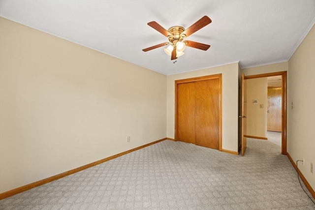 unfurnished bedroom featuring baseboards, a closet, light colored carpet, ceiling fan, and ornamental molding