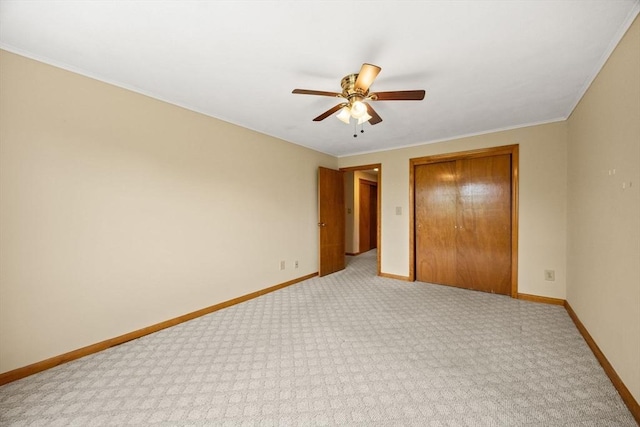 unfurnished bedroom featuring a closet, light colored carpet, baseboards, a ceiling fan, and crown molding