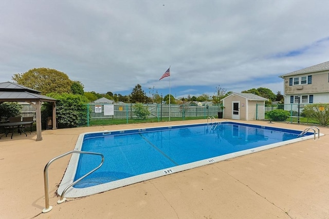 community pool featuring a gazebo, fence, a patio, and an outbuilding