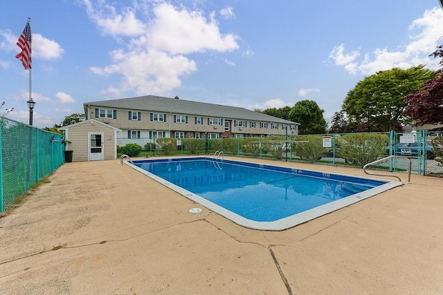 community pool featuring fence, an outbuilding, a storage unit, and a patio area