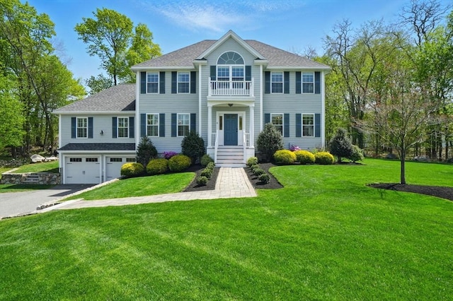colonial house featuring roof with shingles, driveway, a front yard, and a garage