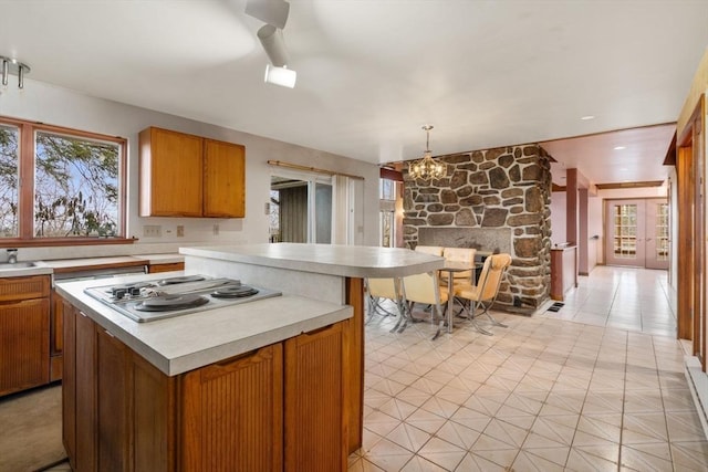 kitchen with a notable chandelier, brown cabinets, stainless steel electric stovetop, and light countertops