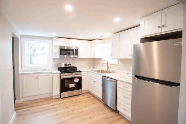 kitchen with stainless steel appliances, light wood-type flooring, white cabinets, and a sink