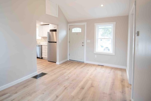 foyer entrance with light wood-style flooring, visible vents, vaulted ceiling, and baseboards