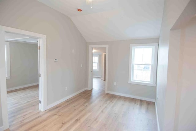 spare room featuring lofted ceiling, light wood-style flooring, and baseboards