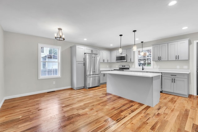 kitchen with light hardwood / wood-style floors, appliances with stainless steel finishes, decorative light fixtures, and plenty of natural light