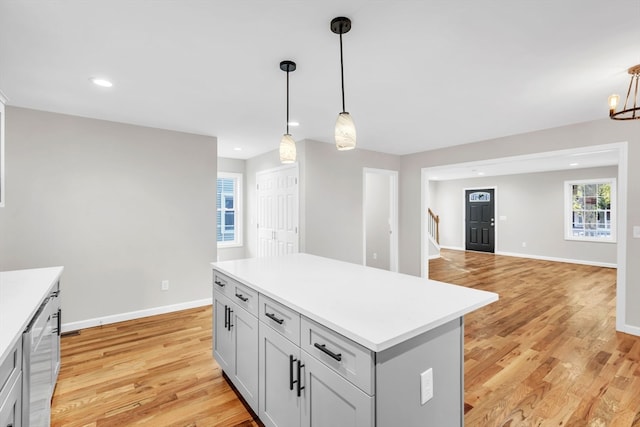 kitchen with stainless steel dishwasher, light wood-type flooring, pendant lighting, a notable chandelier, and a center island