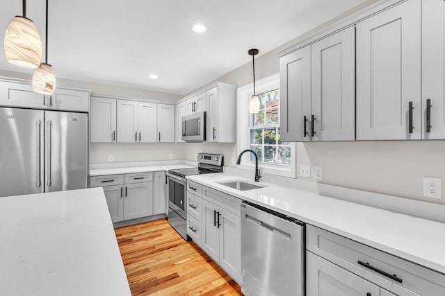 kitchen with stainless steel appliances, sink, light wood-type flooring, and hanging light fixtures