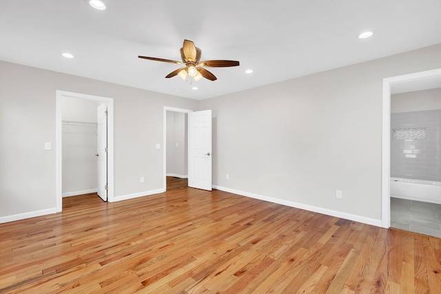 unfurnished bedroom featuring a spacious closet, light hardwood / wood-style flooring, ensuite bathroom, and ceiling fan