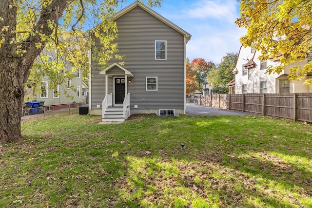 rear view of property featuring central AC unit and a lawn