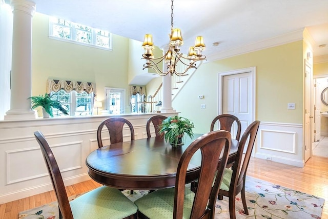 dining area with a decorative wall, an inviting chandelier, light wood-type flooring, ornate columns, and ornamental molding