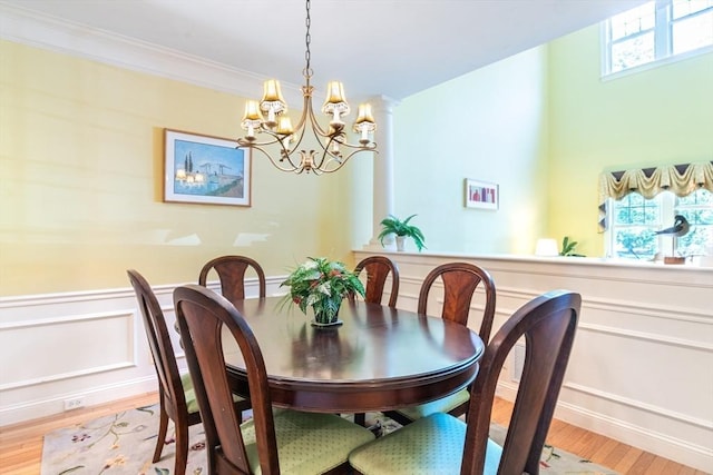 dining area with crown molding, light wood finished floors, an inviting chandelier, and wainscoting