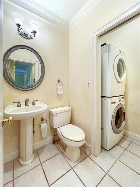 half bath featuring baseboards, ornamental molding, toilet, stacked washer and dryer, and tile patterned flooring
