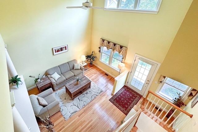 living room with a towering ceiling, a ceiling fan, visible vents, wood finished floors, and baseboards