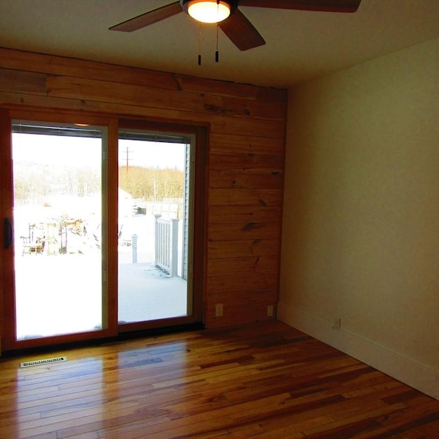 spare room with hardwood / wood-style floors, ceiling fan, and wood walls