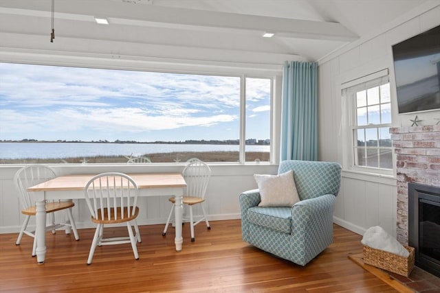 interior space with a brick fireplace, a water view, vaulted ceiling, and hardwood / wood-style flooring