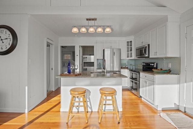 kitchen featuring sink, stainless steel appliances, an island with sink, decorative light fixtures, and white cabinets