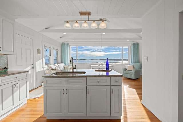 kitchen featuring an island with sink, sink, white cabinets, and hanging light fixtures