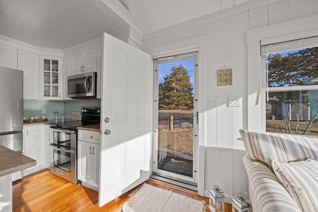 kitchen featuring appliances with stainless steel finishes, backsplash, white cabinets, light hardwood / wood-style floors, and lofted ceiling