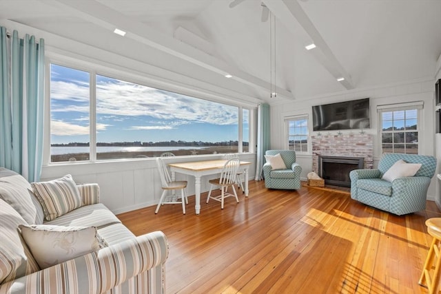 living room featuring plenty of natural light, a water view, lofted ceiling, and a brick fireplace