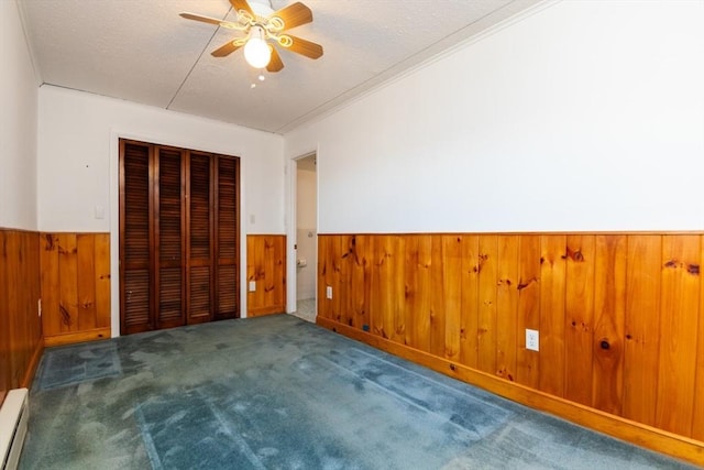 unfurnished bedroom featuring a wainscoted wall, a baseboard heating unit, wood walls, carpet flooring, and a closet