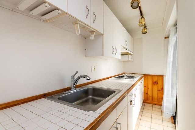 kitchen featuring tile countertops, under cabinet range hood, a sink, white cabinets, and white electric cooktop