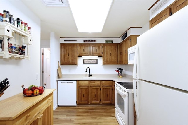 kitchen featuring light wood-style flooring, brown cabinetry, light countertops, and white appliances