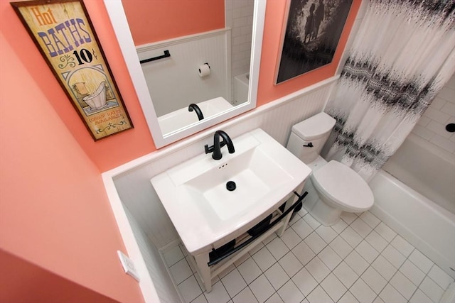bathroom with a sink, toilet, a wainscoted wall, shower / bath combo with shower curtain, and tile patterned floors