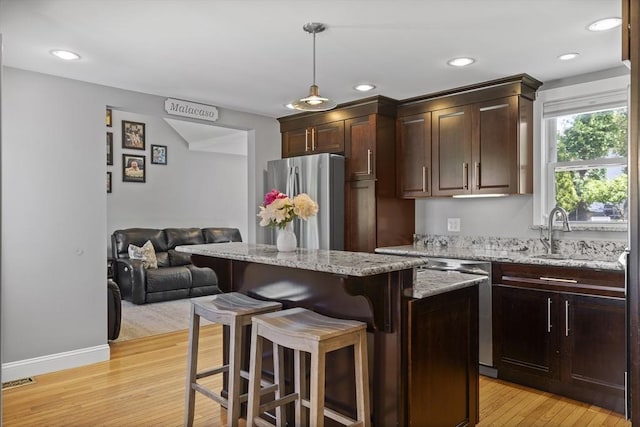 12 Willow St, Wakefield, MA 01880 - kitchen featuring appliances with stainless steel finishes, light wood finished floors, a breakfast bar area, light stone counters, and a center island