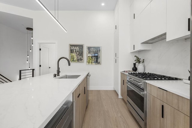 kitchen with light stone countertops, white cabinetry, sink, stainless steel appliances, and light wood-type flooring