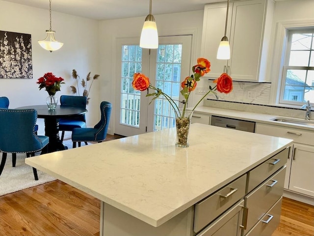 kitchen featuring a center island, light wood finished floors, backsplash, a sink, and dishwashing machine