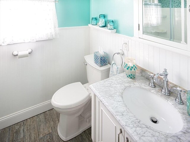 bathroom featuring vanity, wood finished floors, toilet, a wainscoted wall, and a tile shower