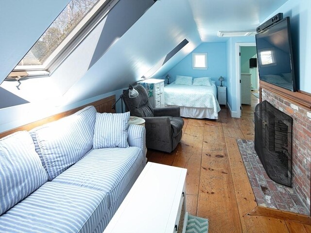 bedroom featuring vaulted ceiling with skylight, a fireplace, and hardwood / wood-style floors