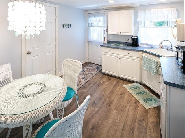 kitchen with dark wood-style flooring, dark countertops, white microwave, white cabinetry, and a sink
