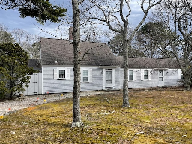 cape cod-style house featuring a shingled roof and a chimney