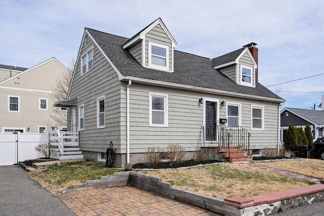 new england style home with fence, a front yard, a patio, a chimney, and a shingled roof
