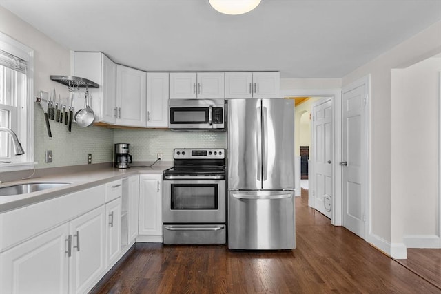 kitchen with backsplash, appliances with stainless steel finishes, a sink, light countertops, and white cabinetry