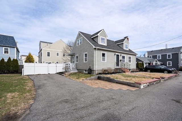 new england style home with fence, a shingled roof, and aphalt driveway