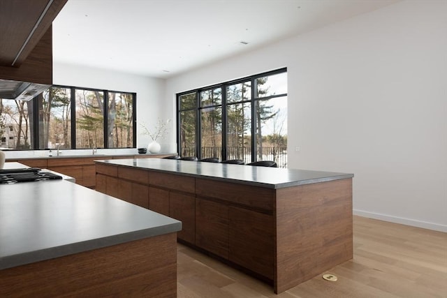 kitchen with baseboards, light wood-style flooring, a kitchen island, modern cabinets, and light countertops